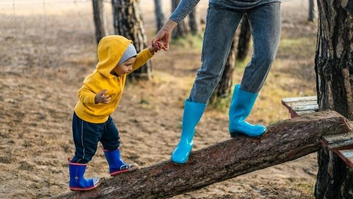 A young boy balancing on a log with an adults support